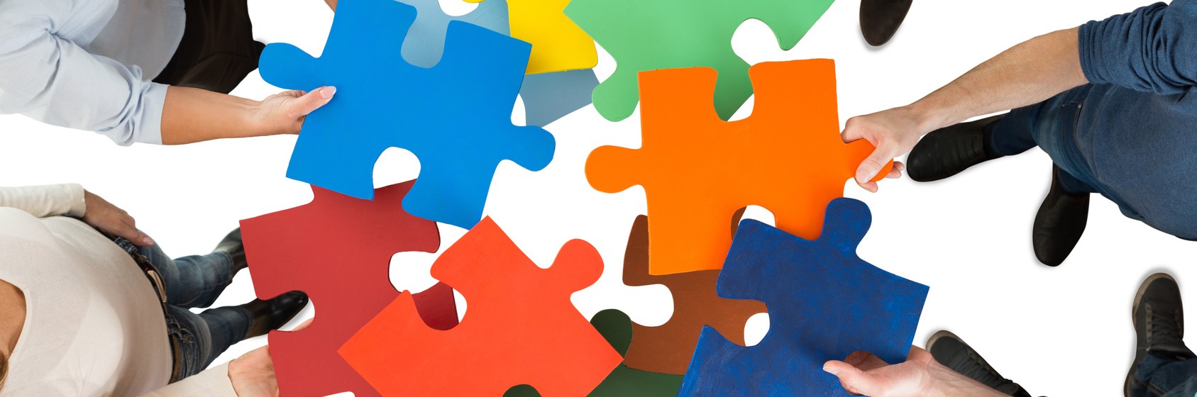 Directly above shot of people holding colorful puzzle pieces in huddle against white background